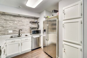 A modern kitchen with white cabinets, a stainless steel refrigerator, a microwave, and a stone backsplash. - 4 Mi to Dtwn: Gem w/ Pool Access & Patio in Austin (Austin)