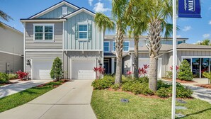 A two-story house with a front garage, a well-maintained lawn, and a palm tree. - 7 Mi to European Village: Pond-front Townhome! (Palm Coast)