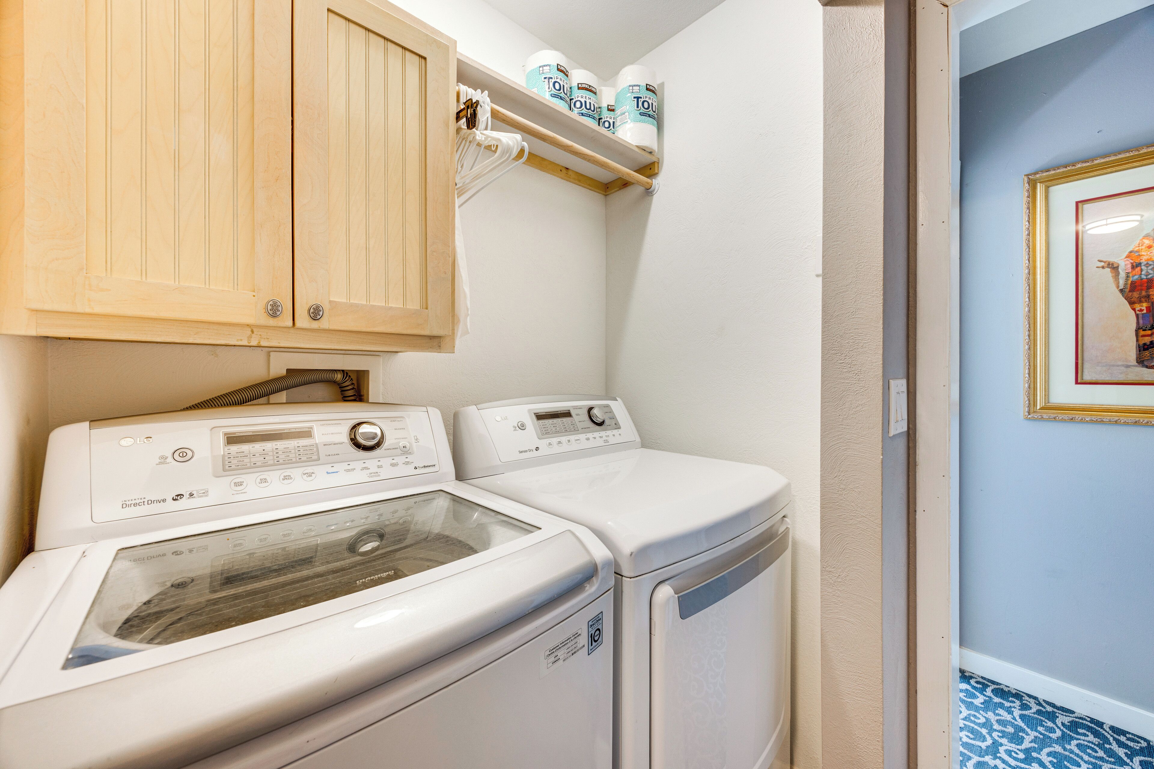 A laundry room with two front-loading washing machines, a wooden cabinet above, and a shelf with toilet paper.