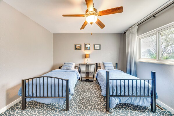 Une chambre avec deux lits simples, un ventilateur de plafond, une table de chevet et une fenêtre avec des rideaux.