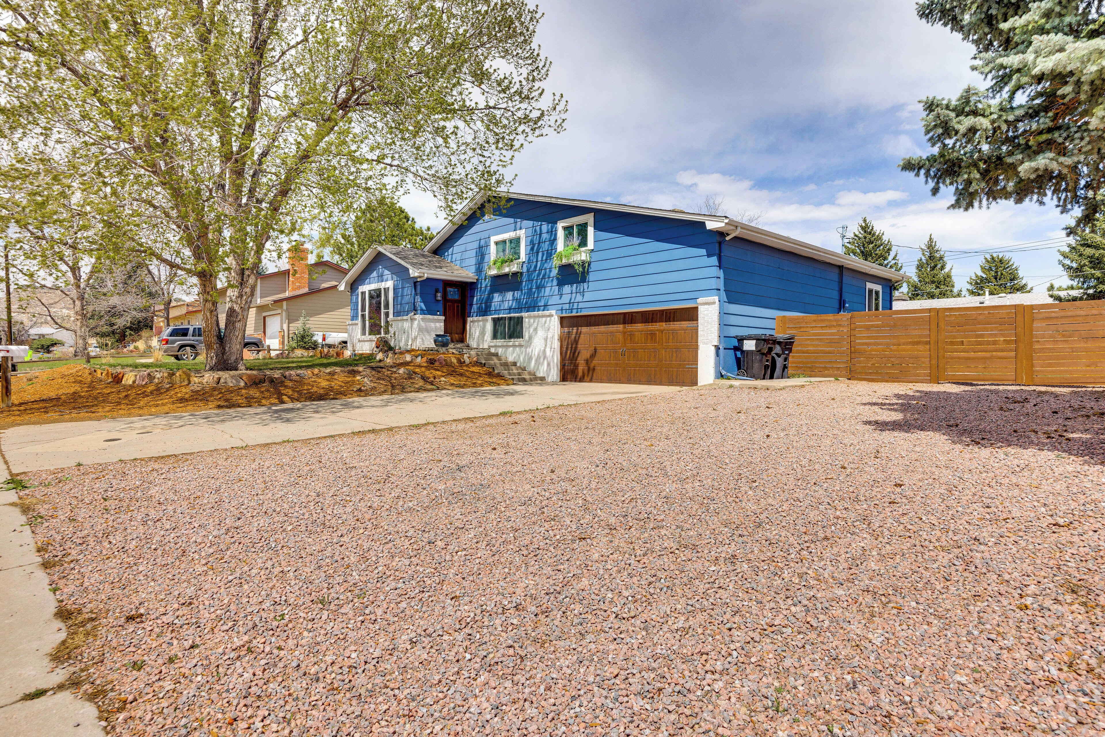 A residential house with a blue exterior, a wooden garage door, and a gravel driveway.