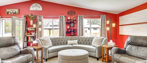 Una sala de estar con sofá modular, sillones de cuero, un otoman redondo, una estantería y un adorno en la pared.