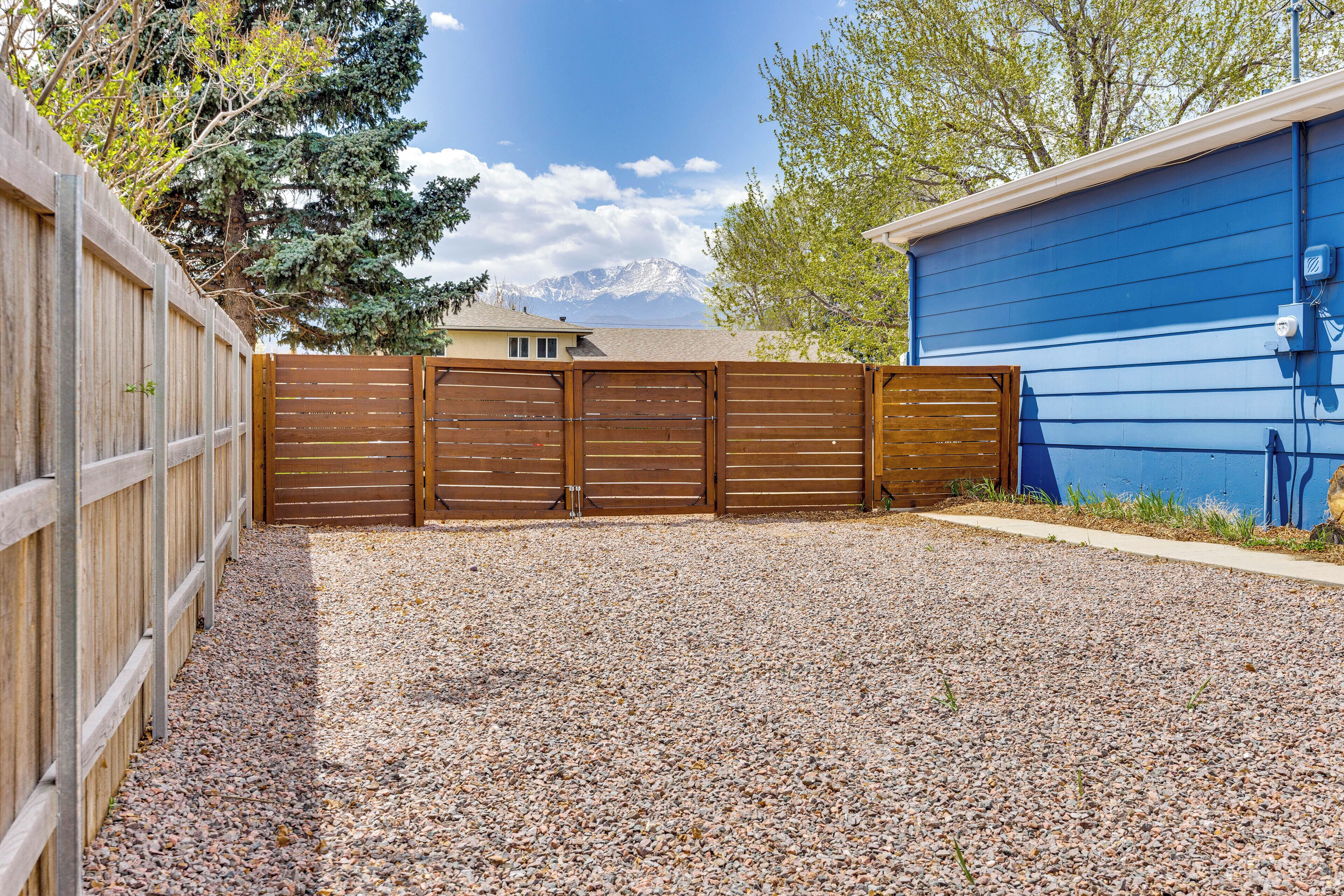 A fenced backyard with a gravel driveway and a blue building.