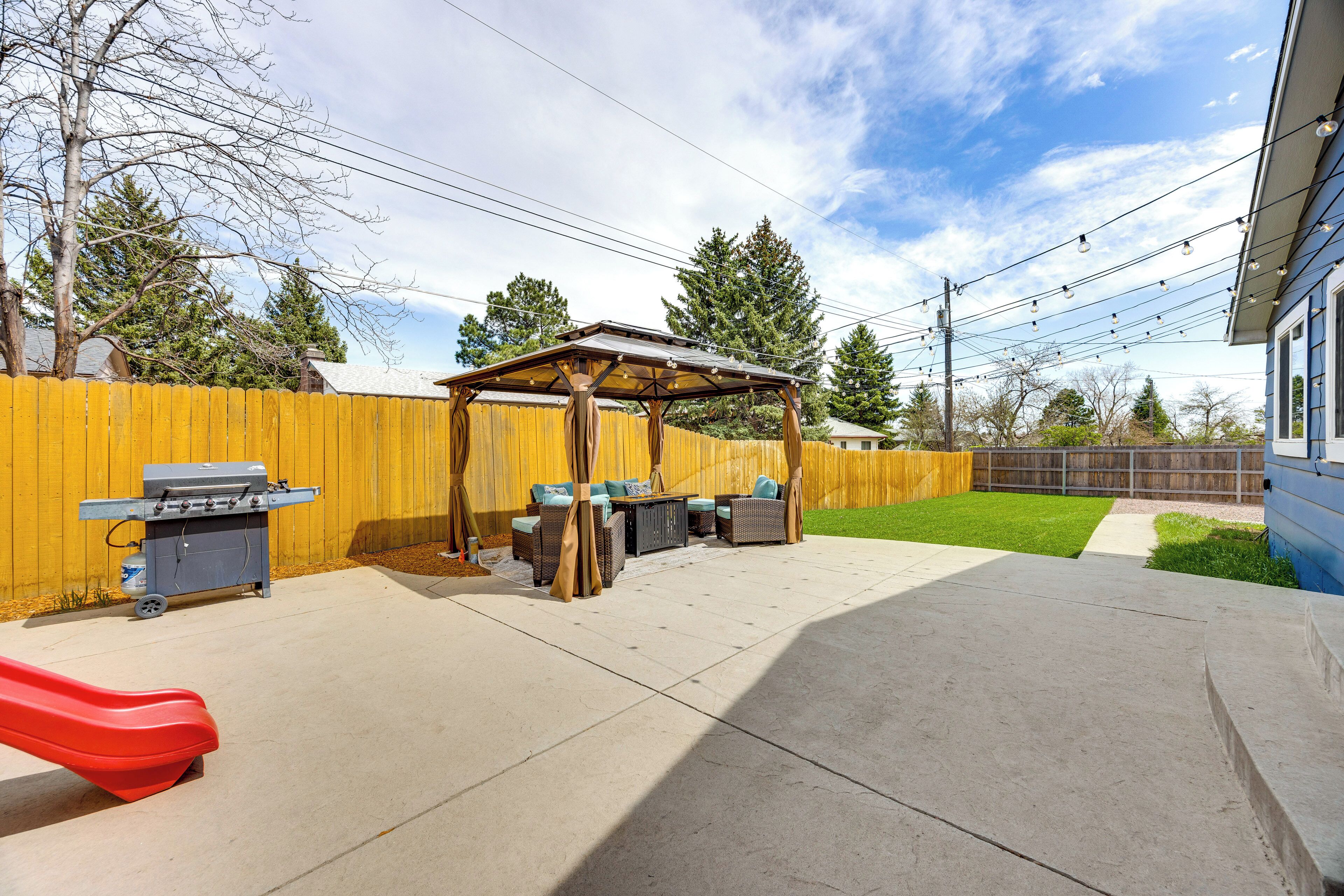 Un patio trasero con zona de barbacoa, mobiliario exterior y un tobogán.