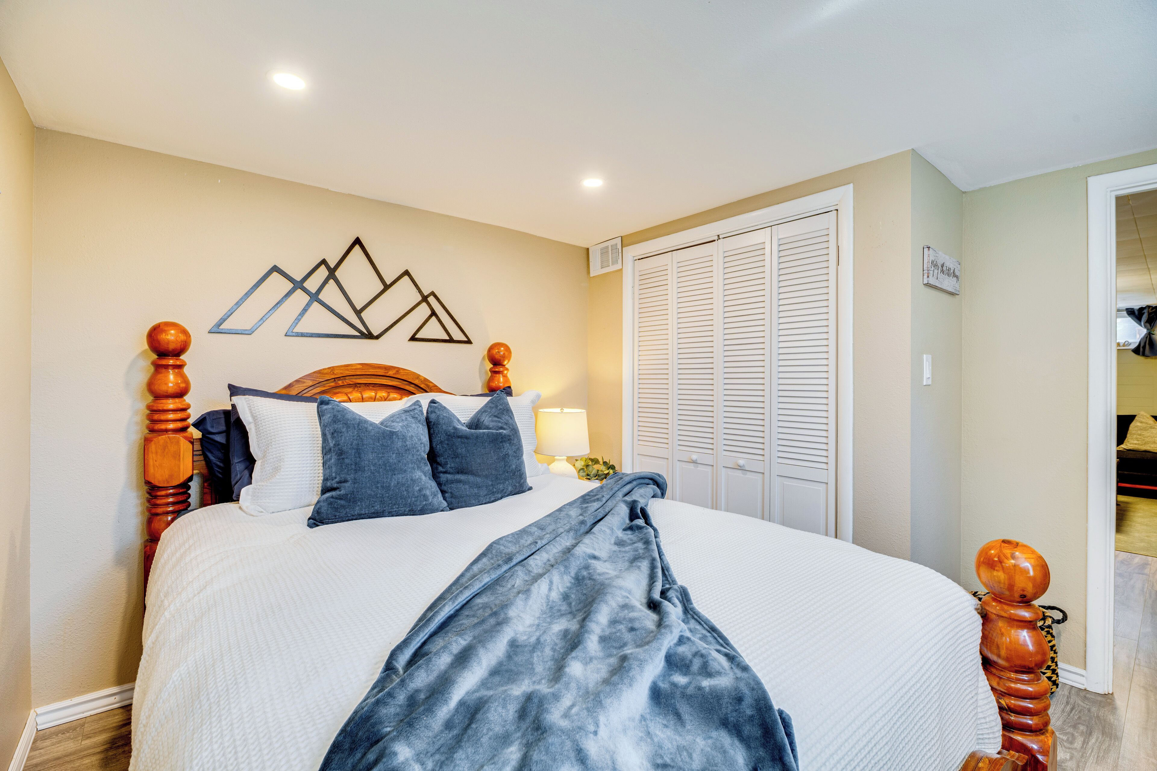 A neatly made bed with a wooden headboard, a blue blanket, and several pillows.