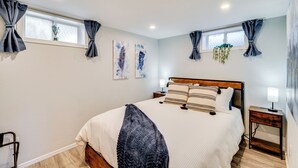 A bedroom with a large bed, two bedside tables, a window with curtains, and wall art.