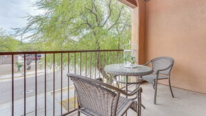 Un balcon avec des fauteuils en osier et une table en verre, donnant sur une rue et des arbres.