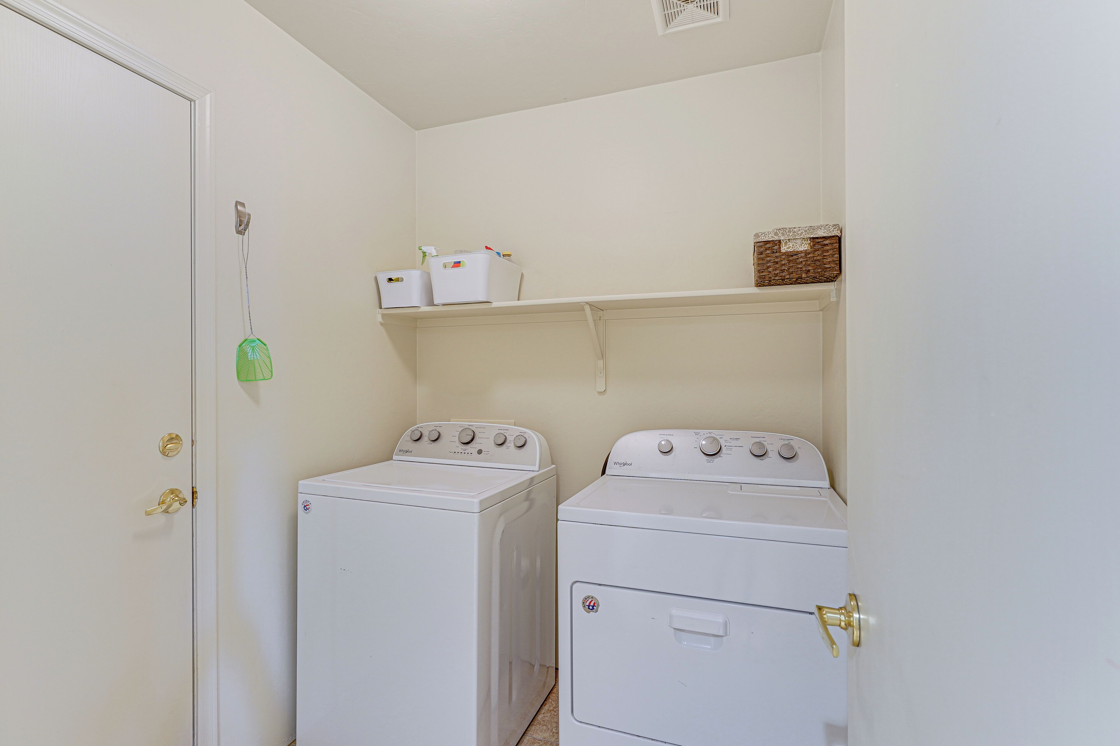 A laundry room with two white washers and dryers, a shelf with baskets, and a door with a brass handle.