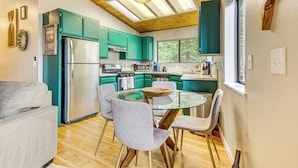 A modern kitchen with teal cabinets, a glass dining table, and a stainless steel refrigerator. - 2 Mi to Lake Arrowhead: Treetop Retreat w/ Deck (Lake Arrowhead)
