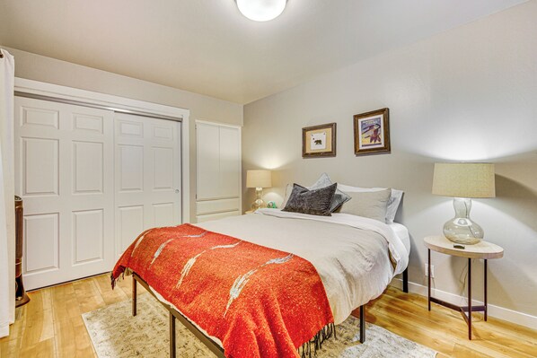 A bedroom with a bed, a nightstand, a lamp, a door, and two framed pictures on the wall. - 2 Mi to Lake Arrowhead: Treetop Retreat w/ Deck (Lake Arrowhead)