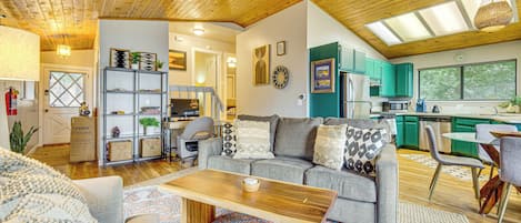 A spacious living area with a wooden ceiling, a grey sofa with patterned cushions, a wooden coffee table, and a colorful rug.