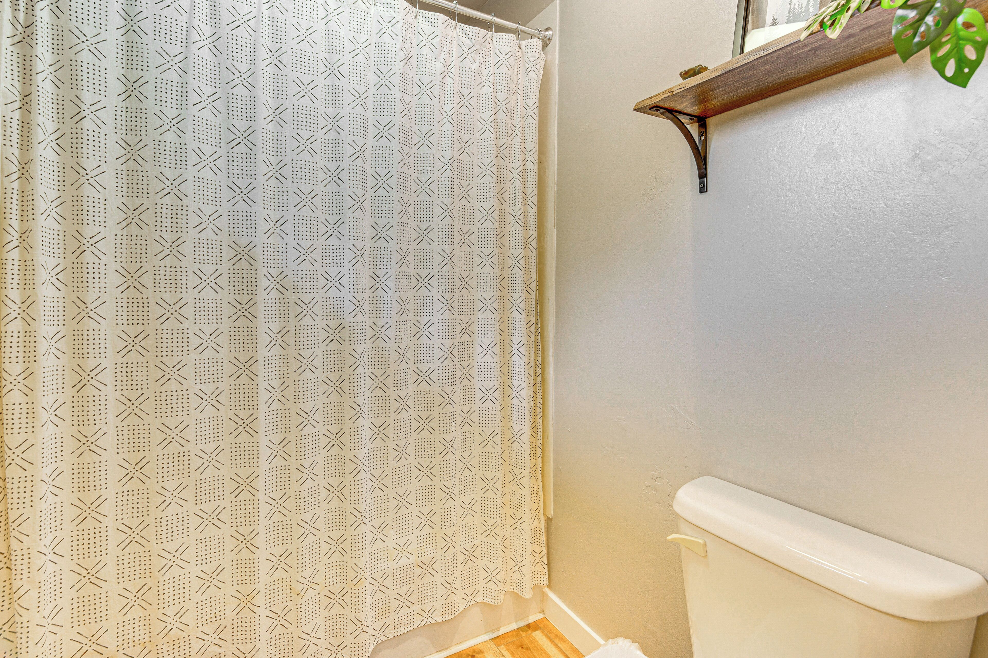 A bathroom with a patterned shower curtain, a toilet, and a wooden shelf with a plant.