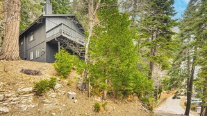 A dark-colored house with a balcony, surrounded by trees and a rocky hillside. - 2 Mi to Lake Arrowhead: Treetop Retreat w/ Deck (Lake Arrowhead)