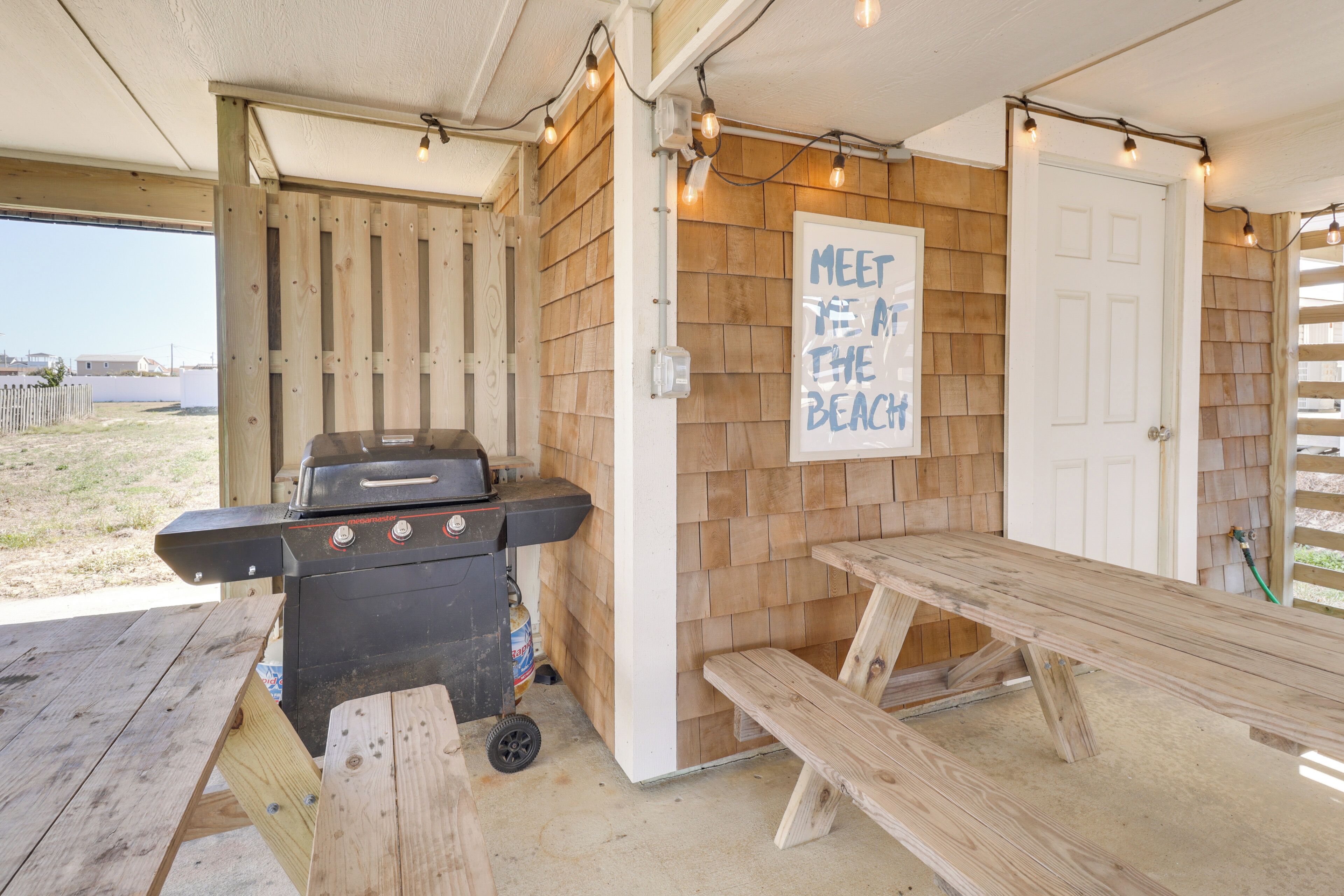 An outdoor patio with a barbecue grill, wooden benches, and a sign that reads "MEET THE BEACH."