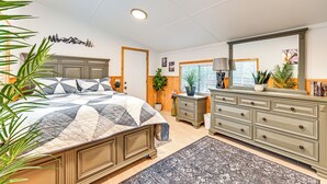 Une chambre avec un grand lit, une commode, un miroir et une fenêtre avec des stores.