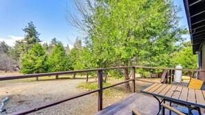 Une terrasse en bois avec une table et des bancs, entourée d’arbres et d’une zone recouverte de gravier.