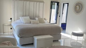 A modern bedroom with a large bed, a bedside table, a chair, a small ottoman, and a round rug. - Contemporary home in Vaison-la-Romaine  Comfort, light & heated pool in Provence (Vaison-la-Romaine)
