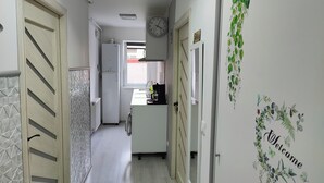 A narrow hallway with a kitchen area at the end, featuring a refrigerator, sink, and a clock on the wall.