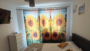 A bedroom with a bed, two pillows, a bedside table, a lamp, and a curtain with a sunflower design.