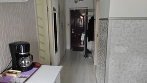 A narrow hallway with a coffee maker on a table, a door with a coat rack, and a patterned wall.