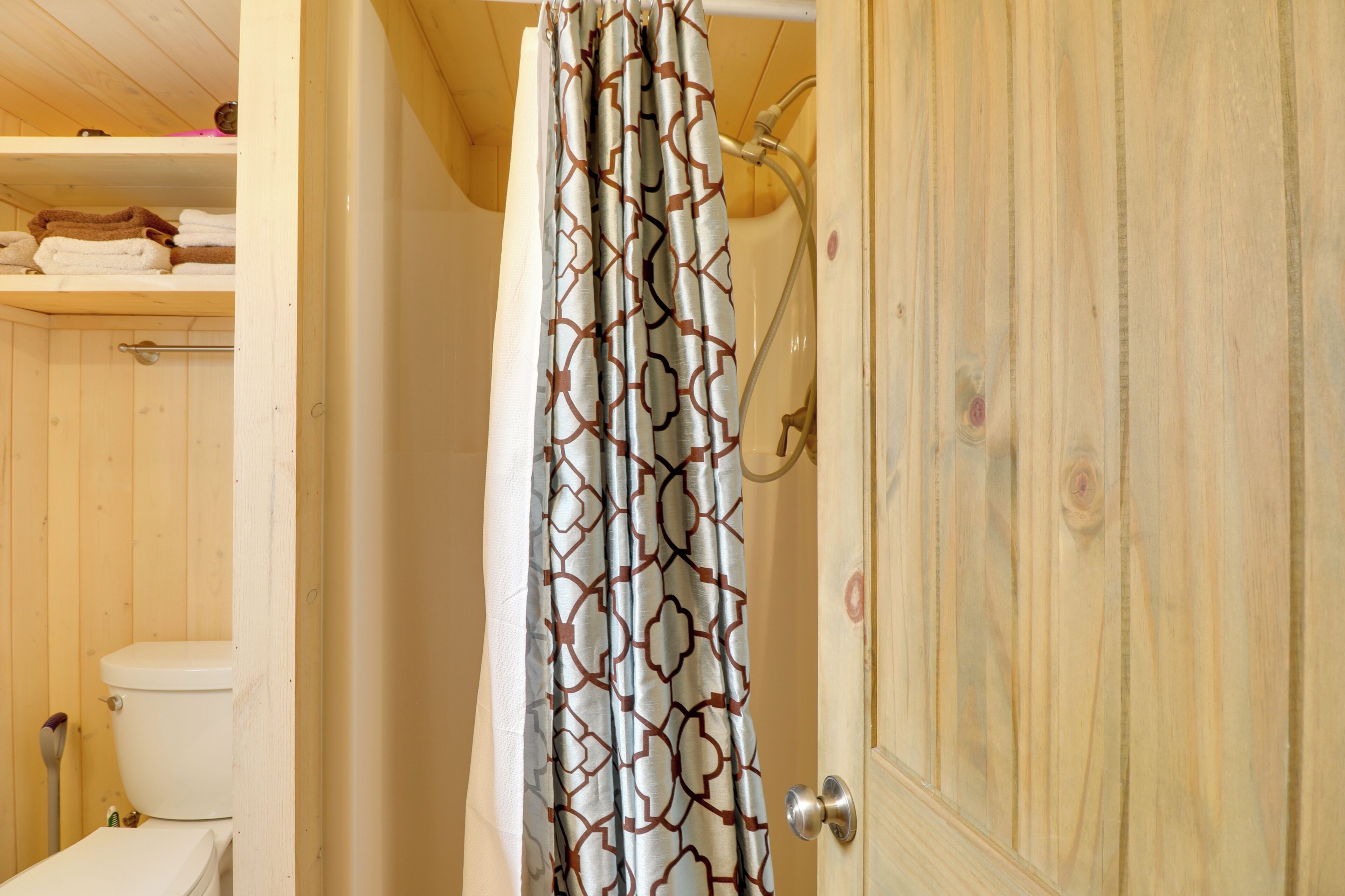 Un baño de madera con inodoro, cortina de ducha y toallero con toallas.