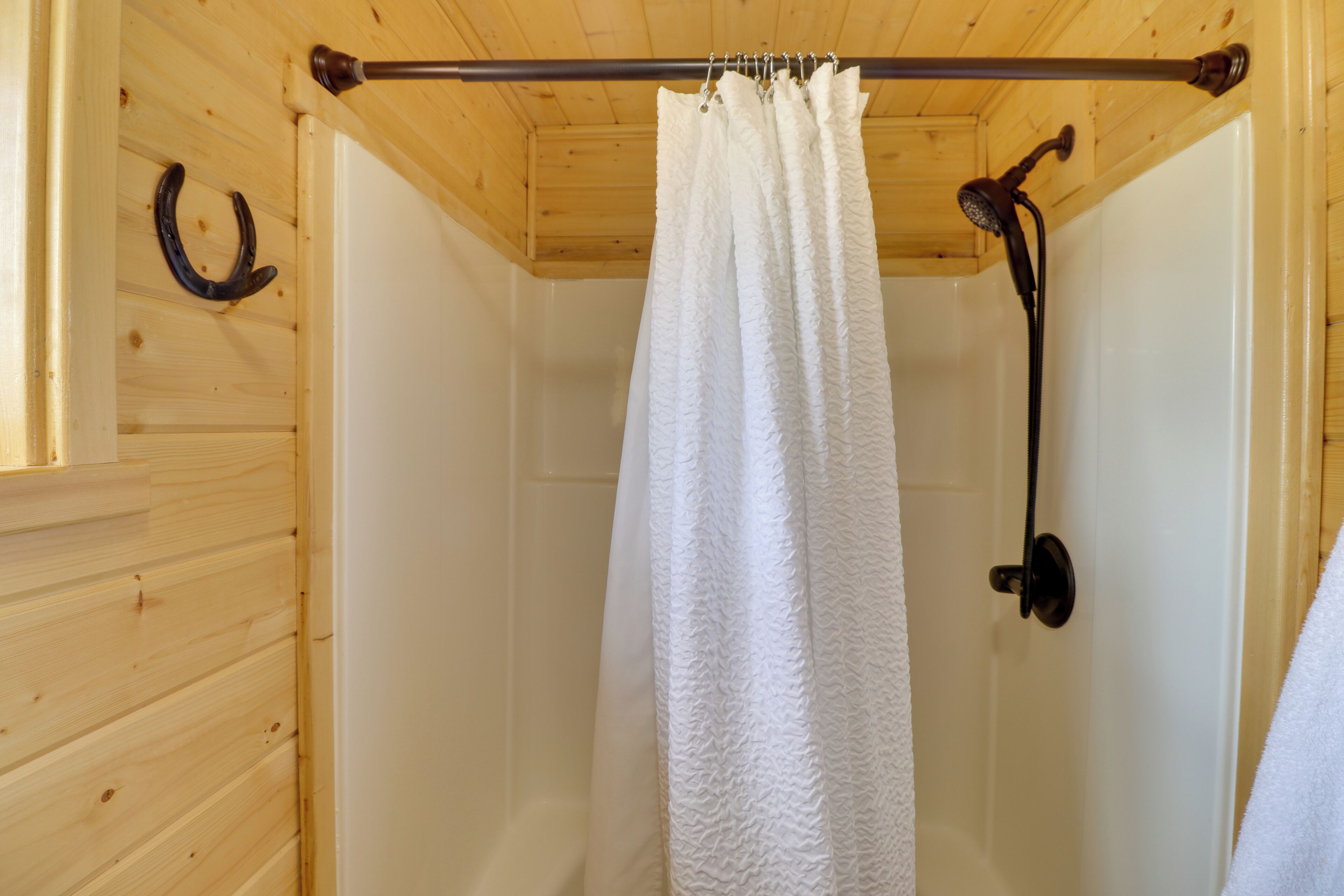 Bany d'una cabana de fusta amb cortina de dutxa, vàter i penjador de tovalloles.