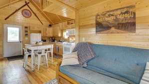 Un acogedor interior de cabaña con detalles de madera, un comedor con mesa y sillas, un sofá y una cocina con microondas y estufa.