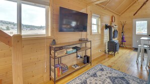 Una cabaña acogedora con una televisión grande, paredes de madera, chimenea y vistas al exterior.