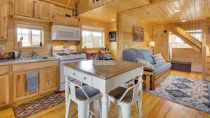 Interior de una cabaña de madera con cocina, comedor y escalera.