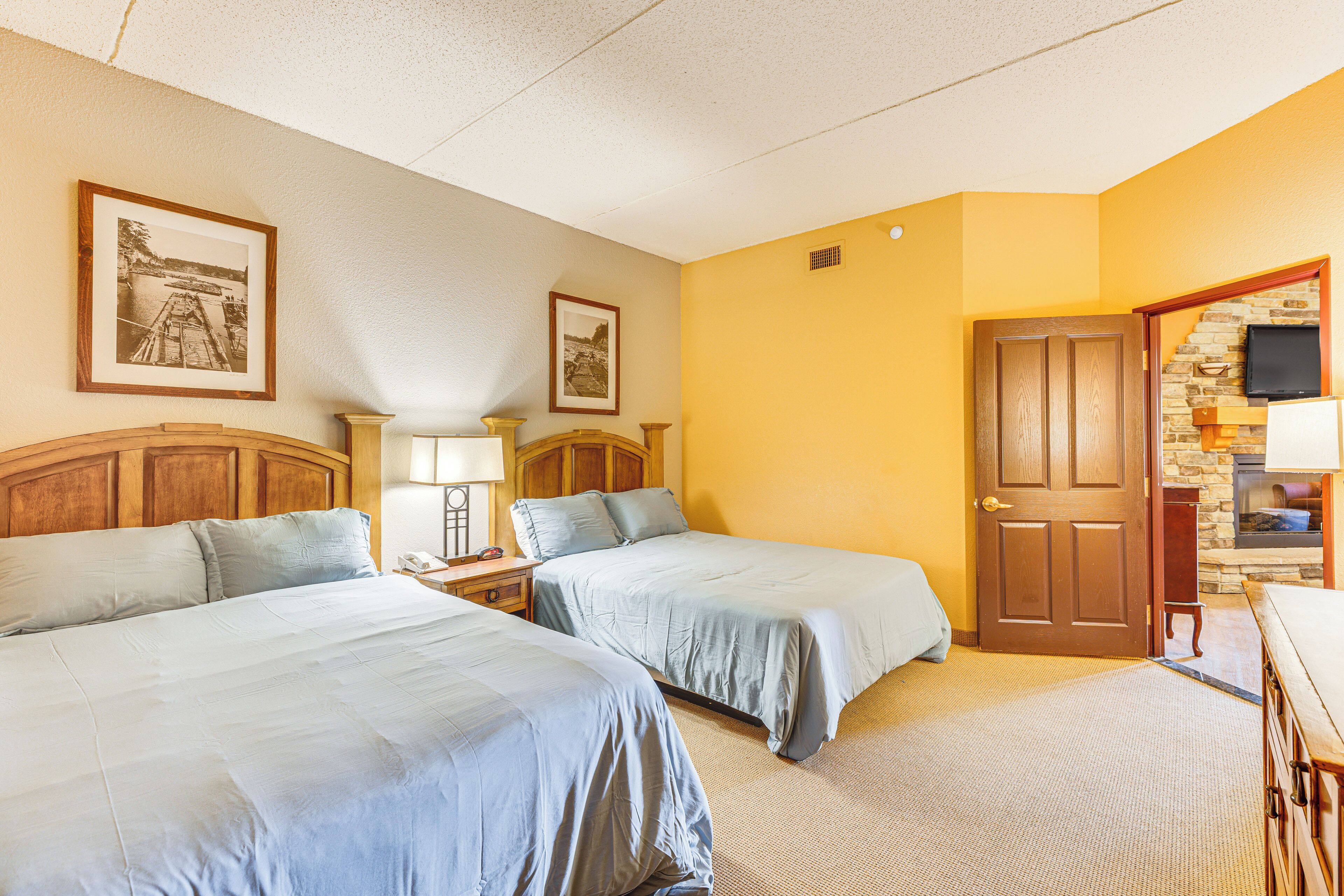 A hotel room with two beds, a wooden headboard, a stone fireplace, and a television.