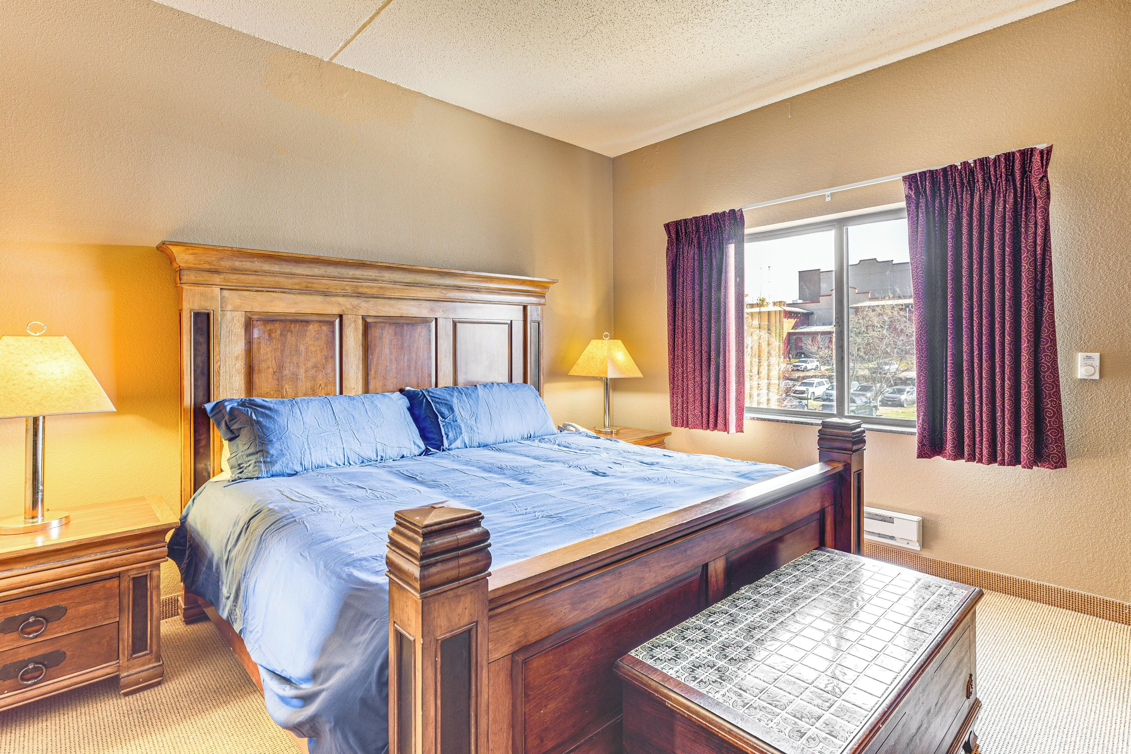 Een netjes opgemaakt slaapkamer met een groot bed, bedlampjes, een raam met gordijnen en uitzicht op de omgeving.