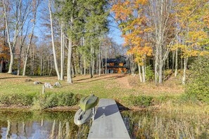 A cabin surrounded by trees with autumn foliage, a dock extending into a pond, and a clear sky. - Private Dock, BBQ Ready: Lakefront Fifield Home! (Park Falls)