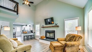 A spacious living room with a fireplace, a television mounted above it, and a kitchen in the background. - 4 Mi to Lake Barkley: Pet-friendly Home w/ Hot Tub (Cadiz)