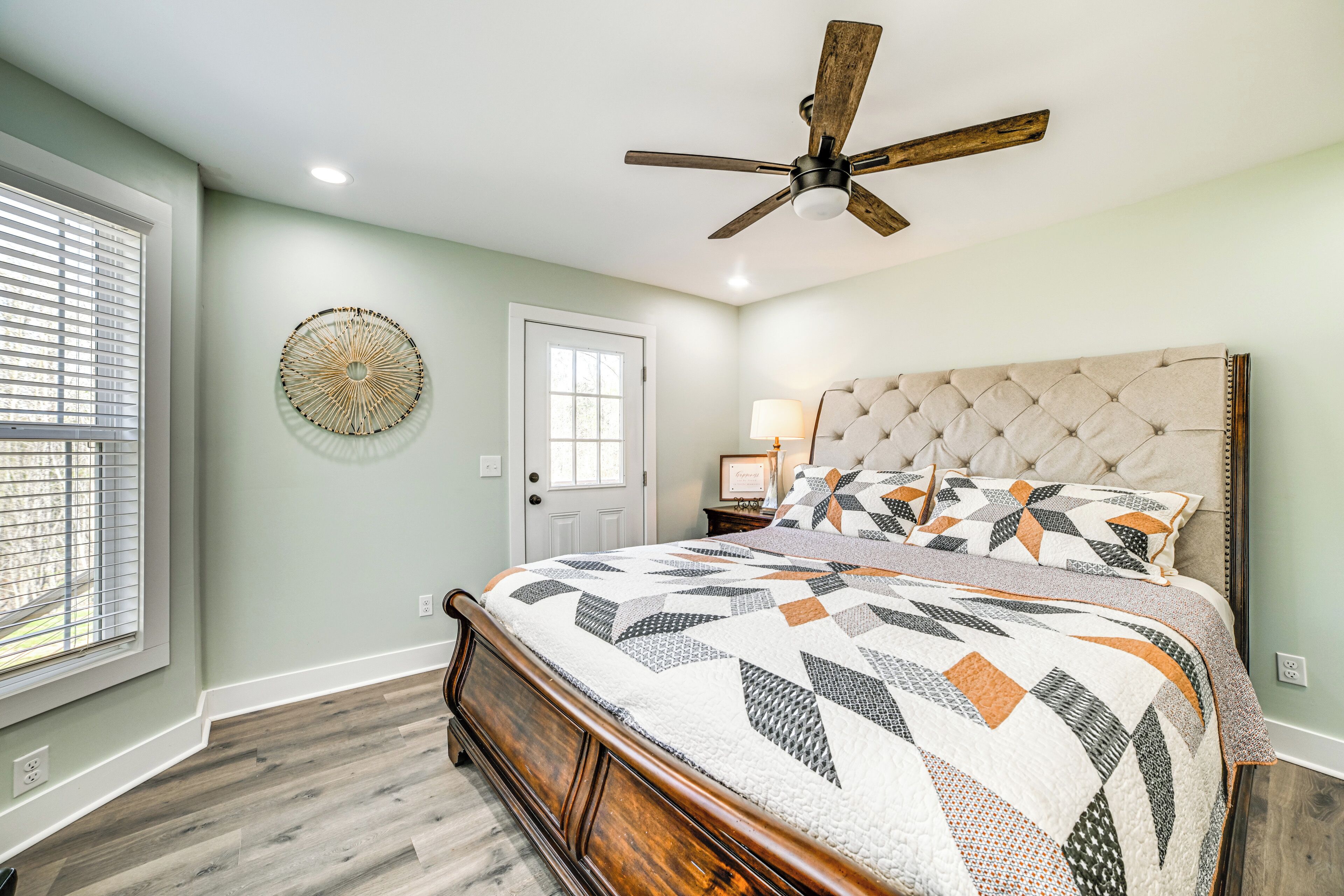 A bedroom with a wooden bed, a ceiling fan, a window with blinds, and a door.