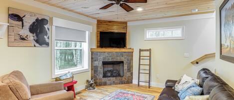 A living room with a fireplace, a ceiling fan, and a large window.
