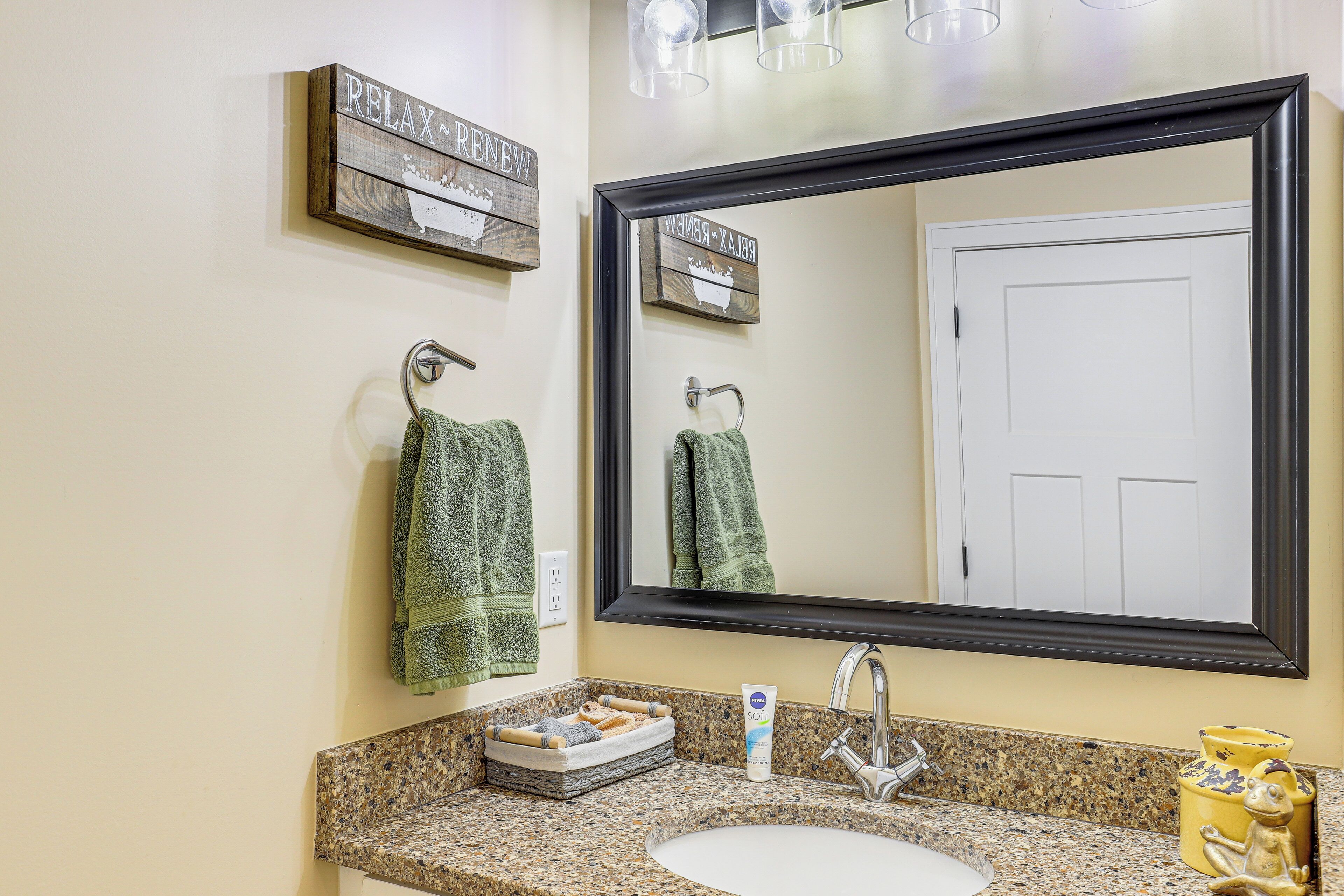 A bathroom with a granite countertop, a white sink, a large mirror, and two towels hanging on hooks.