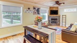 A cozy living room with a fireplace, wooden ceiling, and large windows. - On Farm: Charming Hendersonville Retreat! (Hendersonville)