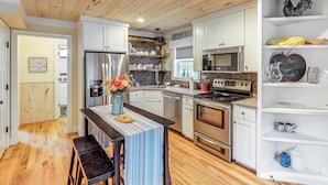 A modern kitchen with wooden flooring, white cabinets, stainless steel appliances, and a central island with a striped tablecloth. - On Farm: Charming Hendersonville Retreat! (Hendersonville)
