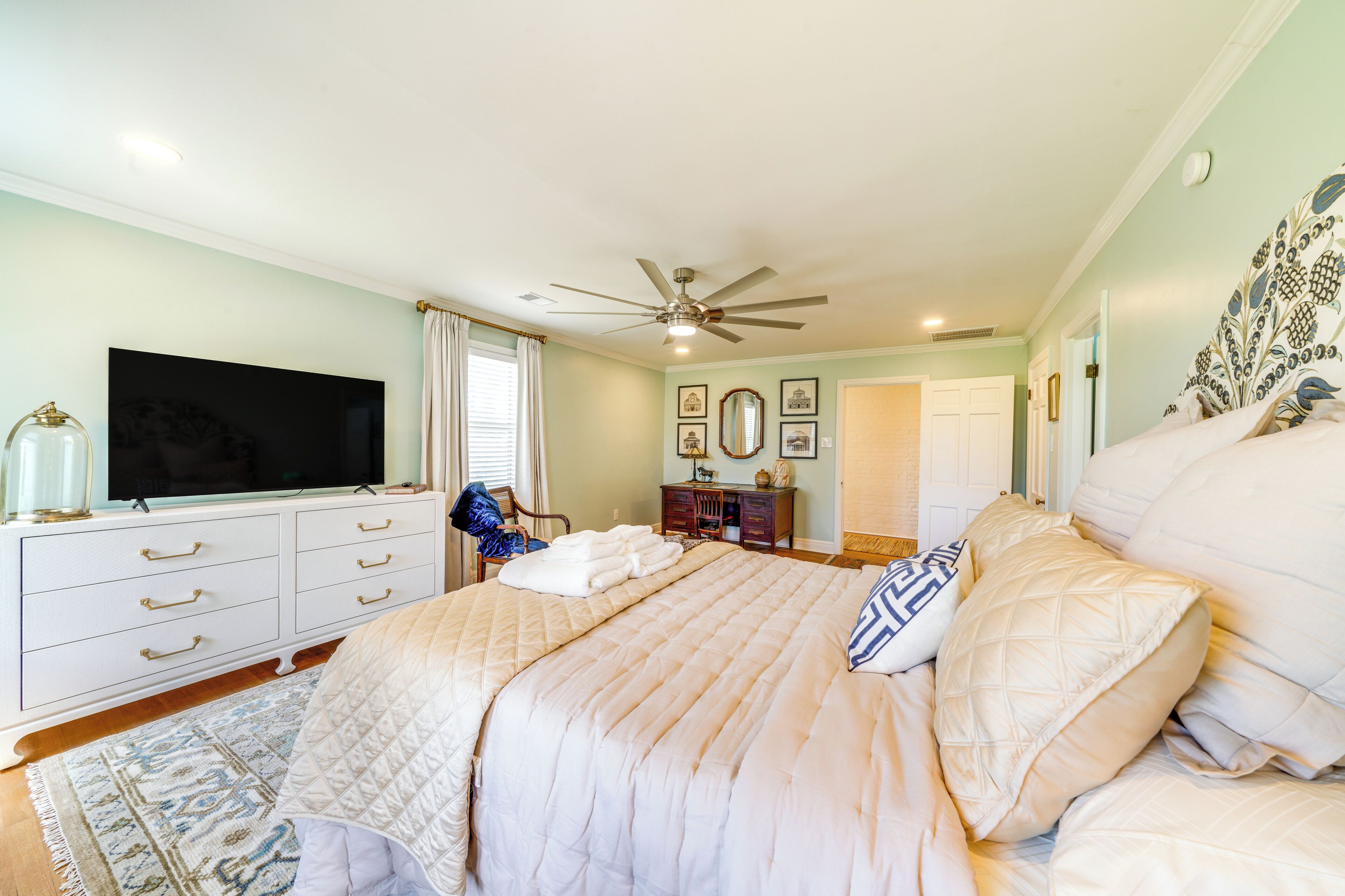 A bedroom with a large bed, a ceiling fan, a TV, a dresser, and a rug.