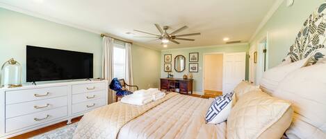 A bedroom with a large bed, a ceiling fan, a TV, a dresser, and a rug.