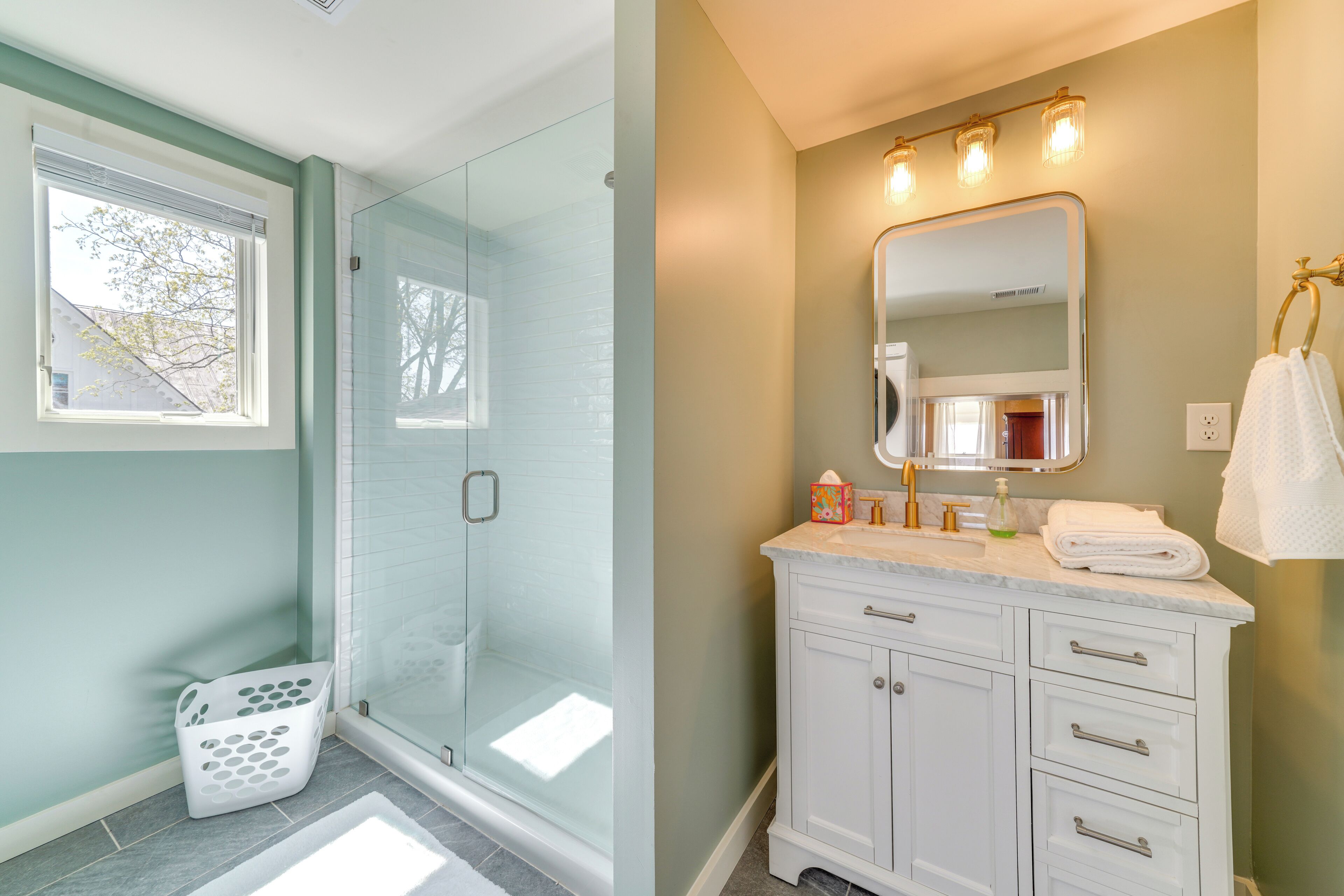 A bathroom with a glass shower enclosure, a white vanity with a mirror, and a window with blinds.