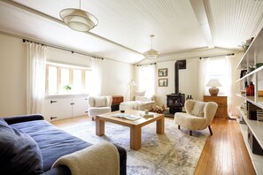 Un salon spacieux comprenant un canapé, un fauteuil et une table basse. On y trouve également une cheminée, une bibliothèque et une fenêtre avec des rideaux.