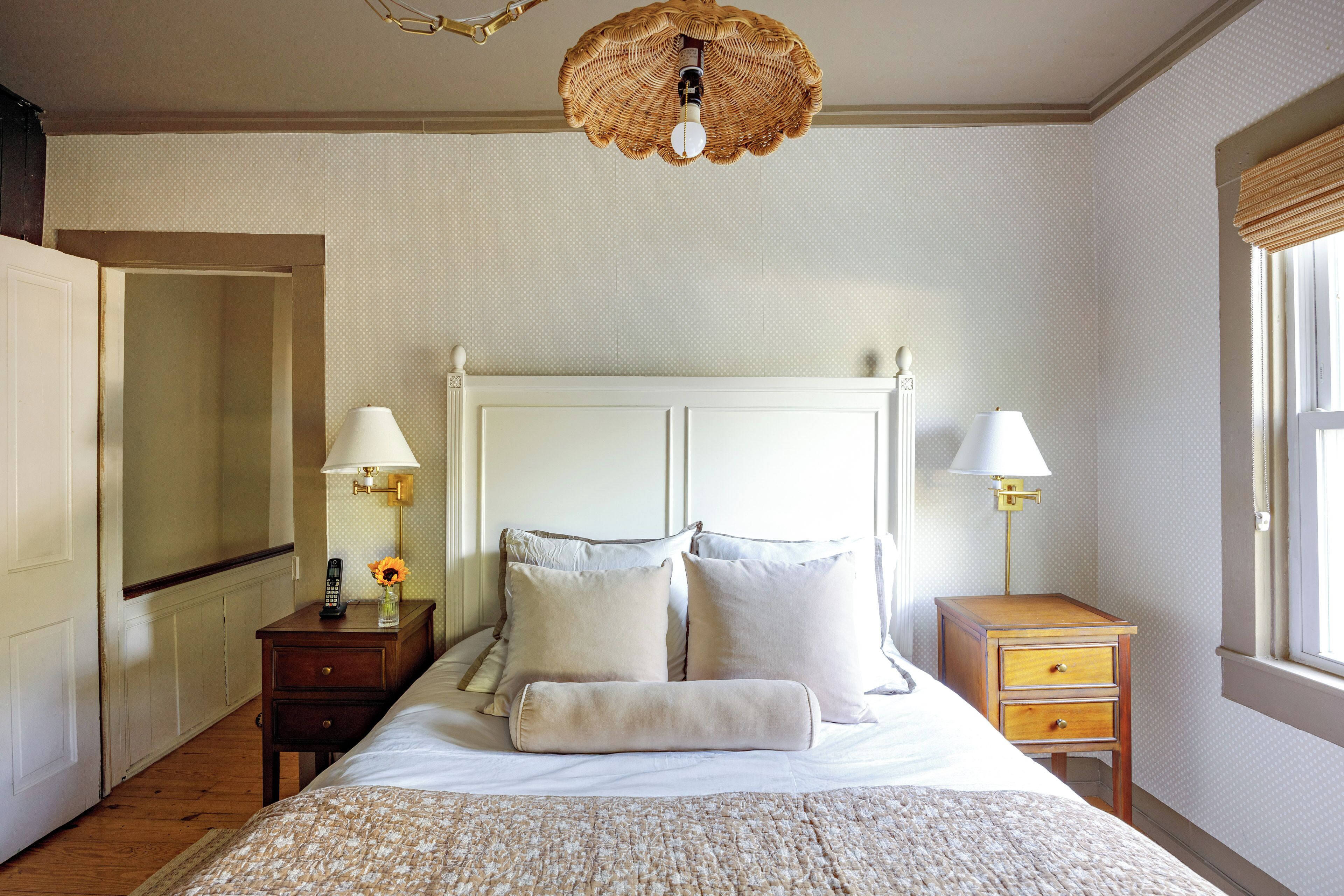 Un dormitorio con cama, dos mesitas de noche, una mesilla auxiliar, una lámpara y un aplique.
