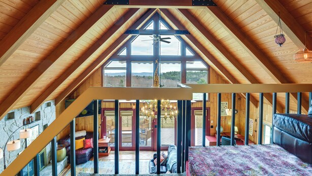Ein geräumiges Dachzimmer mit schrägen Holzbalken, großen Fenstern und Blick ins Freie.