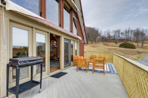 A deck with a grill, chairs, and a view of the surrounding landscape.