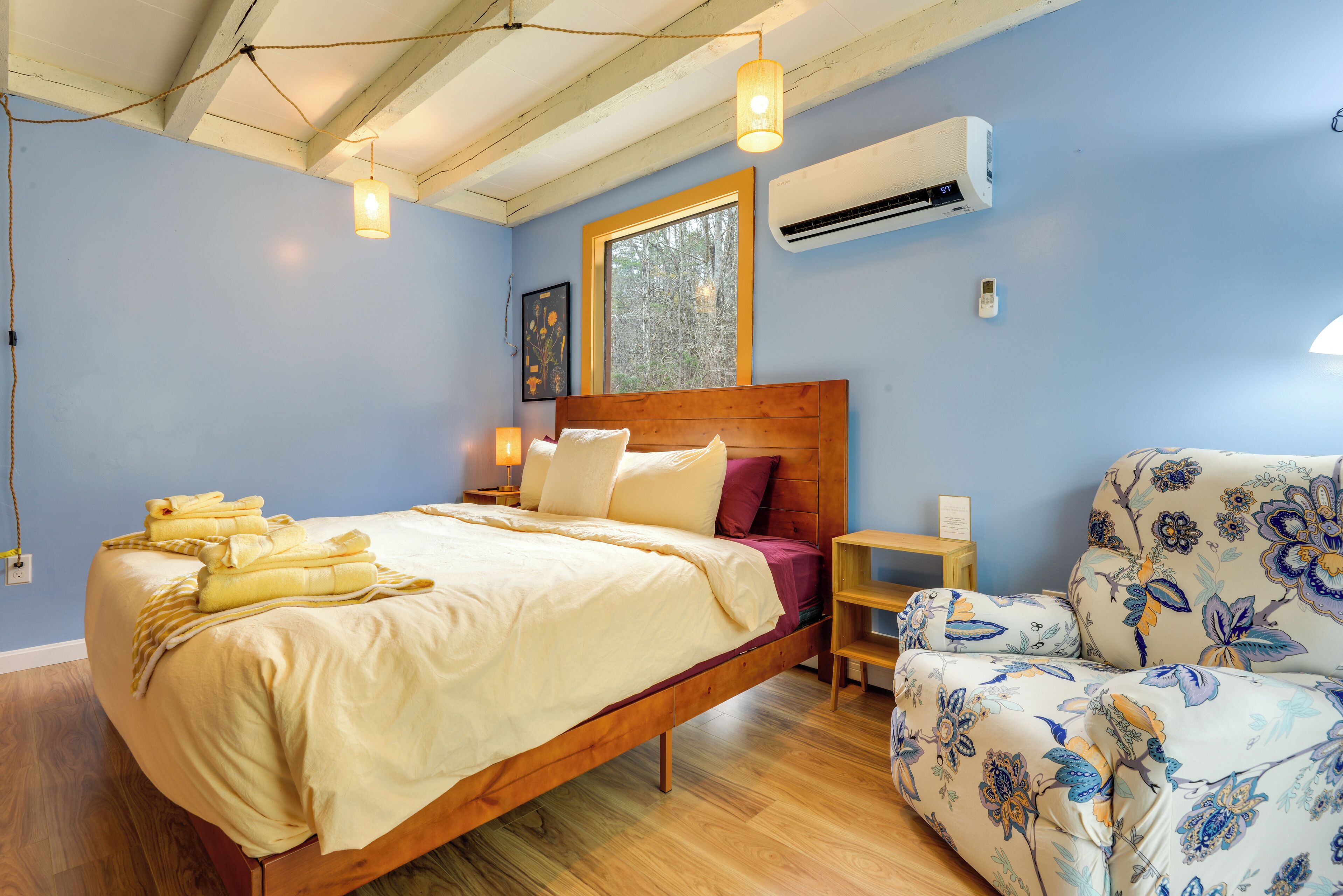Ein Schlafzimmer mit einem hölzernen Bett, einem Nachttisch, einem Sessel mit floralem Bezug und einer Klimaanlage an der Wand.