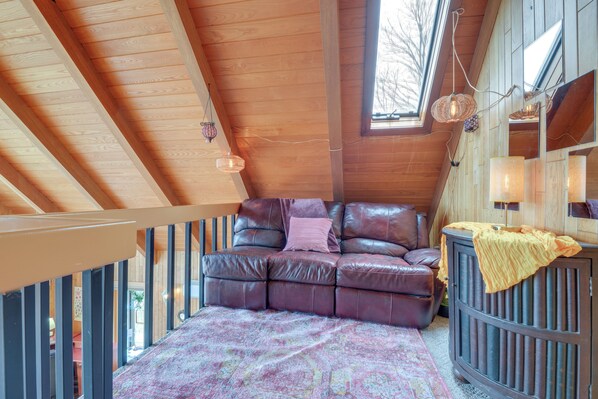 Una habitación acogedora con techo de madera, un sofá de cuero, un tapete estampado y un armario.