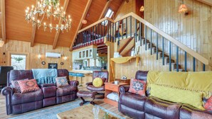 Ein geräumiges Wohnzimmer mit Ledersofas, einer Holztreppe und einem Chandelier.