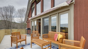 Eine Holzterrasse mit Gartenmöbeln, darunter Stühle und eine Couch, und ein großes Fenster mit Blick auf eine natürliche Landschaft.