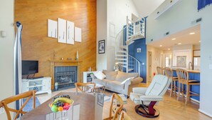 Ein modernes Wohnzimmer mit Holzwand, Kamin, Essbereich mit Glastisch und Treppe zu einer oberen Ebene.